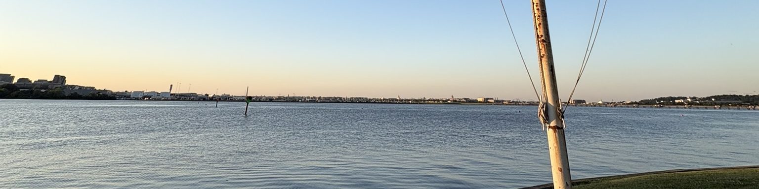 Calm water at golden hour, a low shoreline on the horizon, flagpole at the right